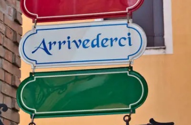 Placa com a palavra 'Arrivederci' em letras azuis, com fundo branco e detalhes em verde e vermelho, representando as cores da Itália.